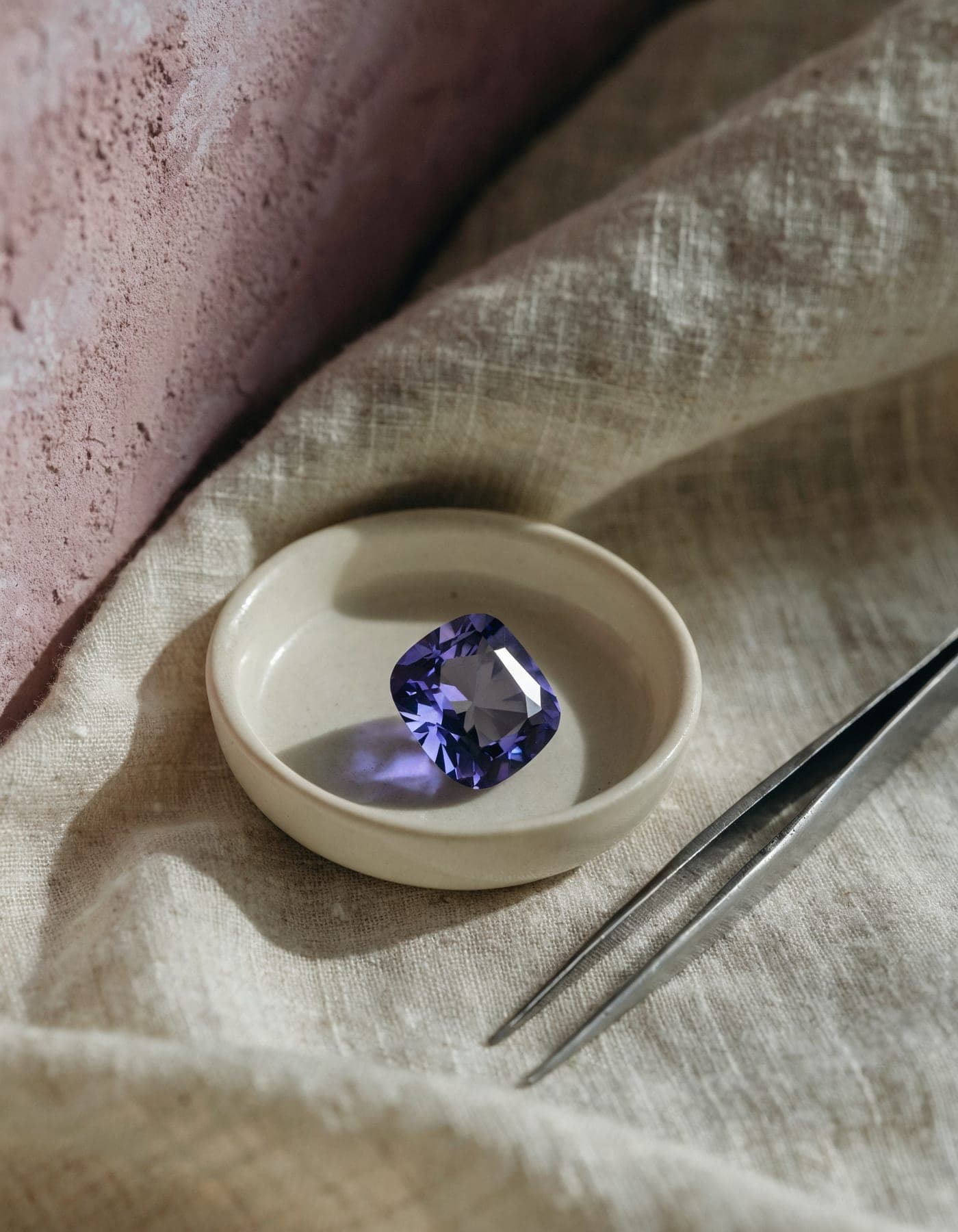 A single natural tanzanite resting in a small dish beside a jeweler’s tweezers, chosen for a bespoke commission.