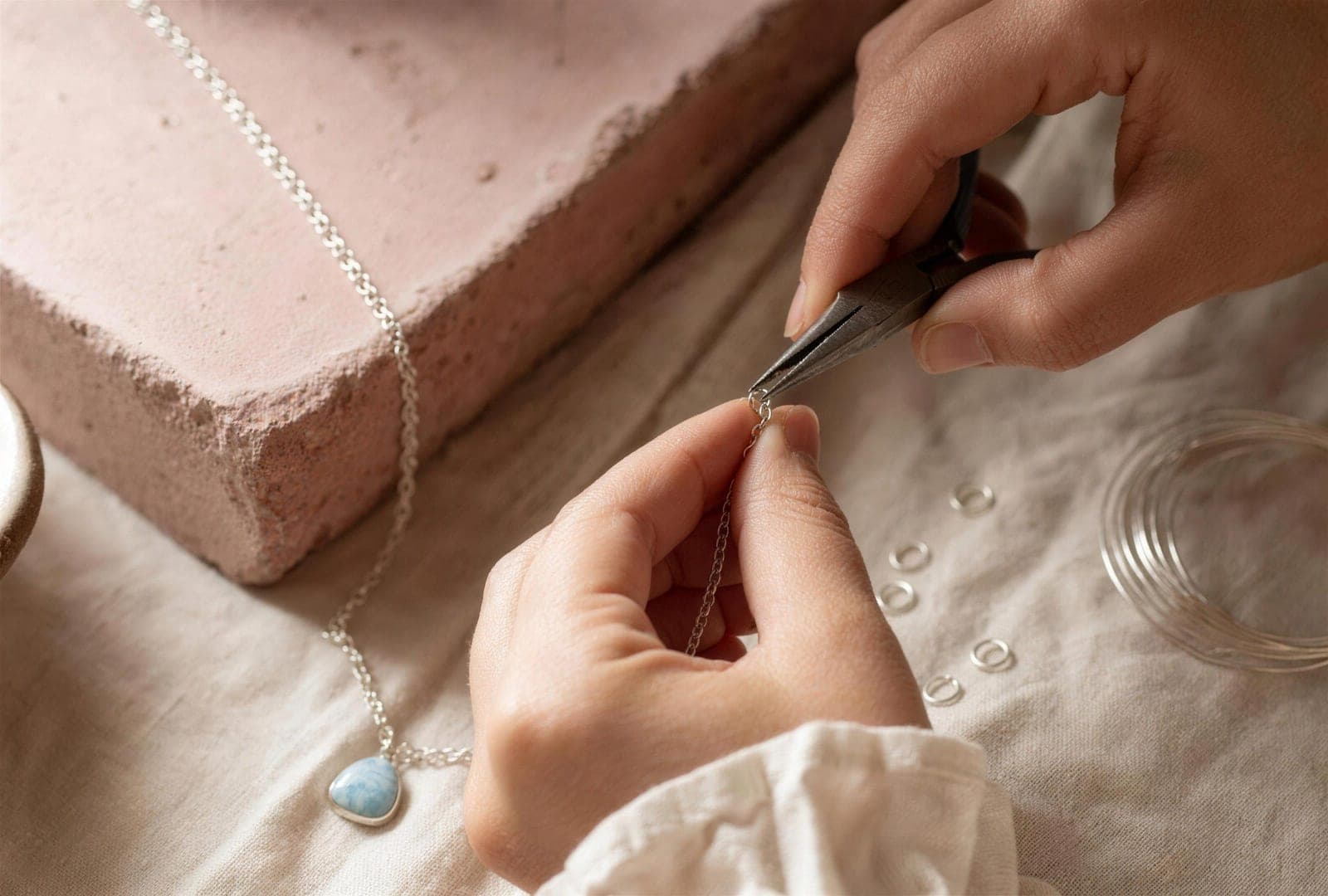 Hands at the jeweler’s bench, using fine pliers to close the last jump ring on a larimar necklace