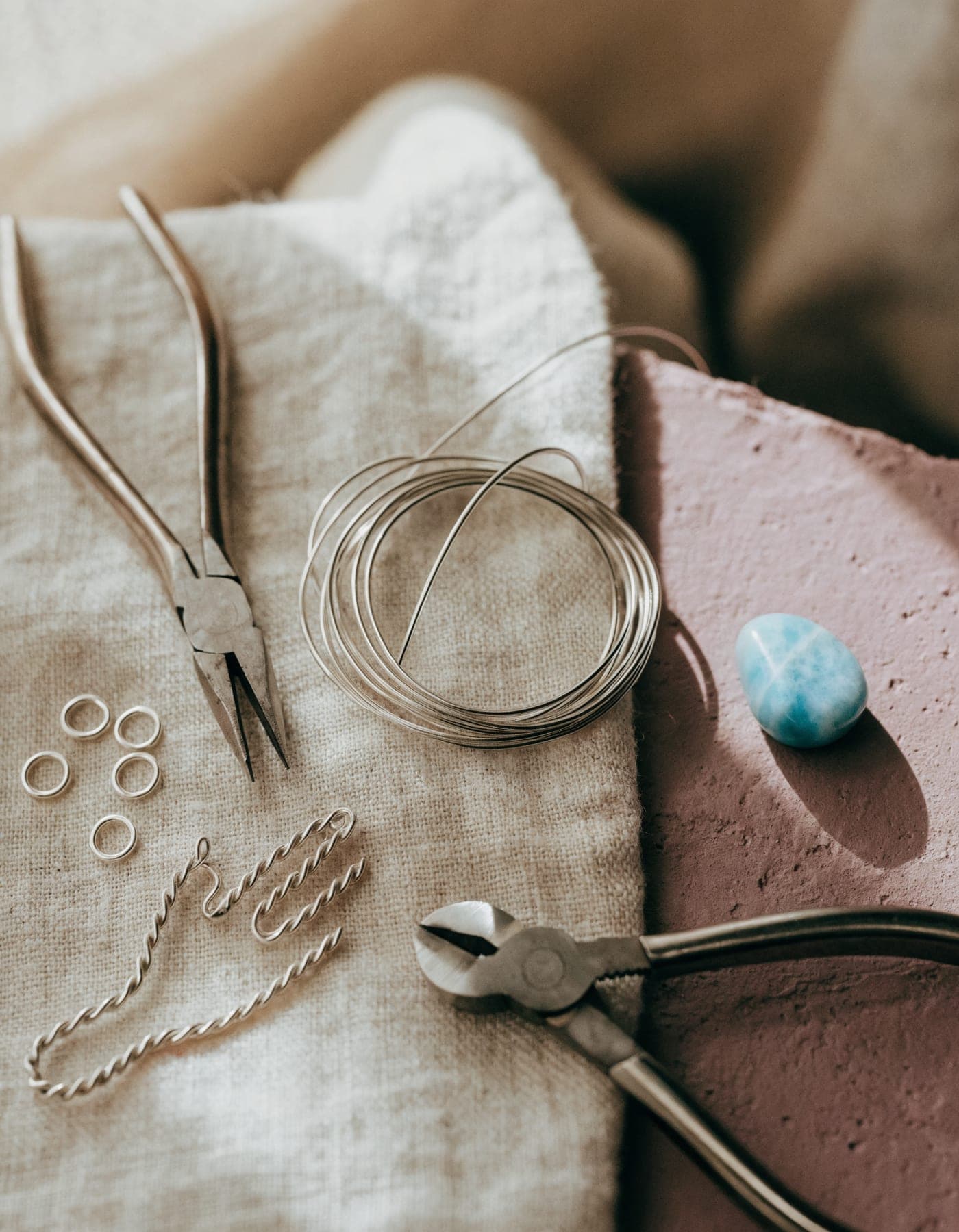 A New York jeweler’s bench — fine pliers, sterling silver wire, jump rings and a larimar stone waiting to be hand-set.