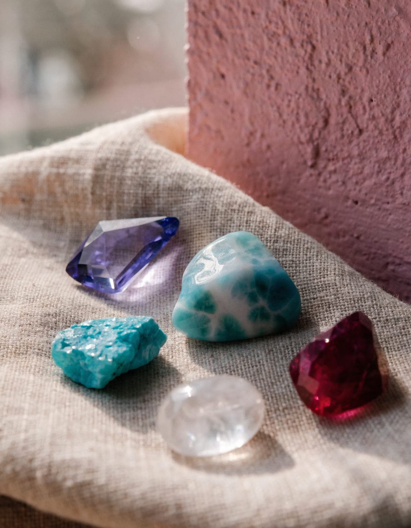 Loose natural gemstones — larimar, tanzanite, turquoise, moonstone and ruby — unset on natural linen, waiting to be chosen.